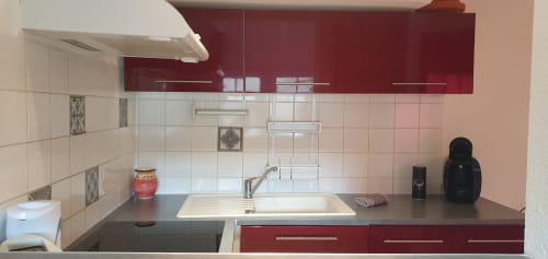 Cuisine moderne dans un appartement de Carcassonne avec armoires bordeaux, carrelage crème, évier inox et électroménagers de comptoir.