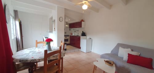 Cosy appartement à Carcassonne avec table à manger, canapé gris, touches de rouge, cuisine ouverte et vue sur le jardin