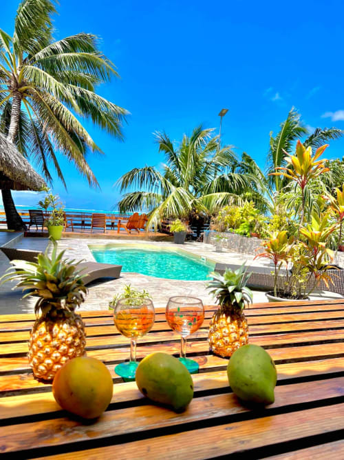 Vue tropicale au bord de la piscine Aimehome avec cocktails, fruits frais, palmiers et océan turquoise
