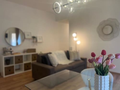Moderno salotto milanese con tulipani rosa, divano, scaffali e luci a soffitto vicino a Bocconi e Duomo