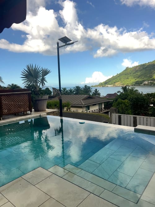 Piscine à débordement avec lampadaire solaire surplombant une baie tropicale à Aimehome Location, resort en Polynésie française avec palmiers et vue océan