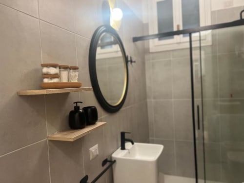 Bagno moderno dell'appartamento A Casa di Imma Milano con specchio rotondo, ripiani in legno, lavabo bianco e doccia con box in vetro