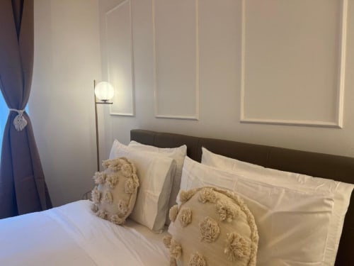 Camera da letto moderna dell'appartamento A Casa di Imma Milano con testata scura, biancheria bianca, cuscini decorativi e lampada da terra
