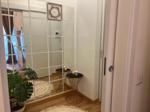 Elegante ingresso di appartamento milanese con parete specchiata, consolle decorativi, pianta in vaso e ghirlanda