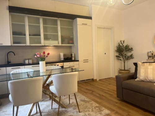 Cucina-soggiorno moderno dell'appartamento milanese con tavolo da pranzo, credenze color crema, top scuri e divano marrone vicino a Bocconi
