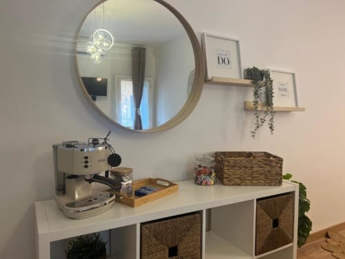 Spazio di lavoro in moderno appartamento a Milano con specchio rotondo, macchina da caffè, mensole sospese con piante e contenitori in vimini