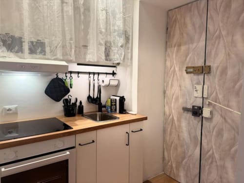 Cucina compatta in appartamento a Milano con piani in legno, maniglie nere, lavello in acciaio inox e portautensili organizzato