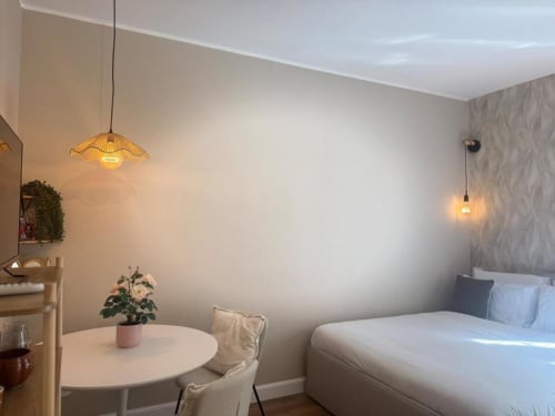 Monolocale moderno a Milano con letto, tavolo rotondo, illuminazione a sospensione e arredamento minimalista vicino ai Navigli e al Duomo.