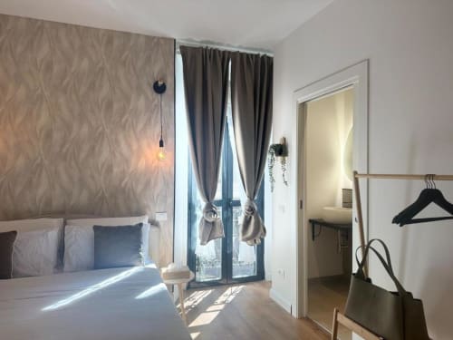 Camera da letto moderna a Milano con luce naturale, letto di design, tende grigie e accesso al balcone vicino al Duomo