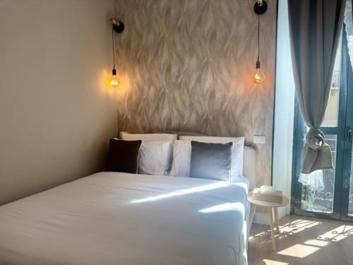 Elegante camera da letto a Milano con lampade a sospensione, carta da parati decorativa, biancheria bianca e accesso al balcone vicino ai Navigli