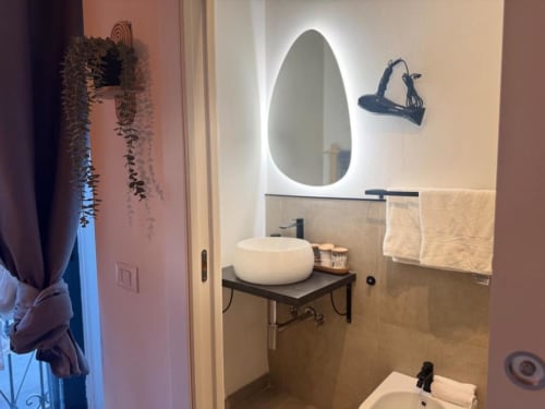 Bagno moderno dell'appartamento A Casa di Imma Milano con specchio a forma di uovo illuminato, lavabo bianco a coppa e portasciugamani