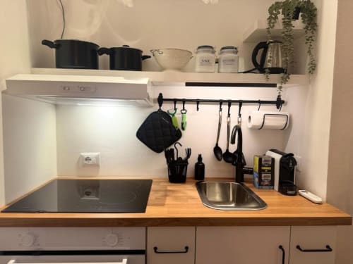 Moderna cucinetta in appartamento a Milano con piano cottura a induzione, lavello, piano in legno e scaffalature a parete organizzate con utensili da cucina