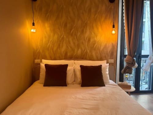 Camera da letto in moderno appartamento a Milano con parete dal finish dorato, luci a sospensione, cuscini bordeaux e vista su balcone verso i Navigli