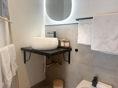 Bagno moderno con lavabo bianco a calice, specchio illuminato, rubinetteria nera e asciugamani bianchi nell'appartamento di Milano vicino al Duomo