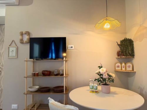 Moderno soggiorno milanese con TV, scaffalature in legno, tavolo rotondo con fiori e lampada a sospensione di design