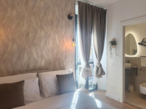 Camera da letto moderna a Milano con carta da parati decorativa, lampada a sospensione, tende grigie e bagno privato vicino ai Navigli