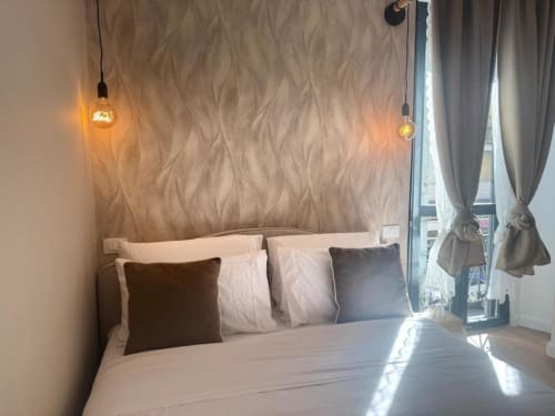 Camera da letto in moderno appartamento milanese con lampade a sospensione, parete texturizzata e vista sulla città vicino ai Navigli e al Duomo