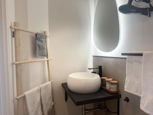 Bagno minimal moderno in appartamento milanese con lavabo bianco, vanity nera, specchio ovale e porta asciugamani in legno