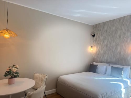 Camera da letto moderna a Milano con letto queen, lampada a sospensione, tavolino rotondo con fiori e parete in rilievo