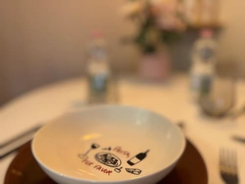 Tavolo apparecchiato nell'appartamento A Casa di Imma Milano con piatto decorativo con motivi di vino e cibo