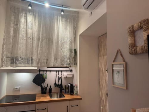Moderna cucina a vista nell'appartamento milanese con lavello in acciaio inox, piano di lavoro in legno e tende in pizzo
