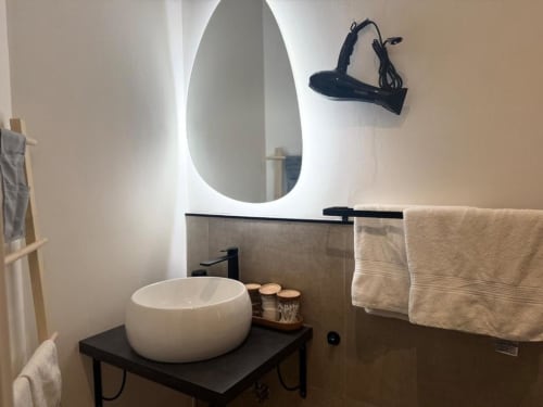 Bagno moderno di Casa di Imma Milano con lavabo bianco a forma di goccia, specchio illuminato e asciugamani beige