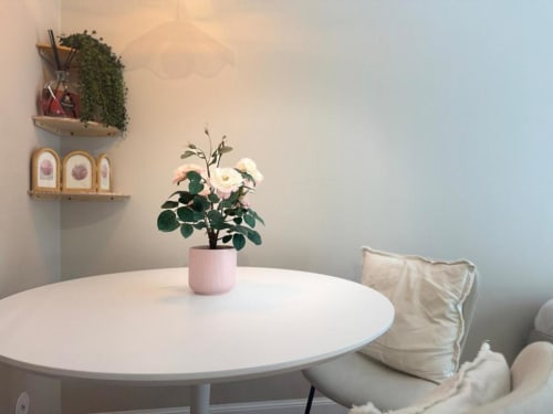 Elegante interno minimalista a Milano con tavolo rotondo bianco, fiori in vasi rosa e mensole decorative a parete