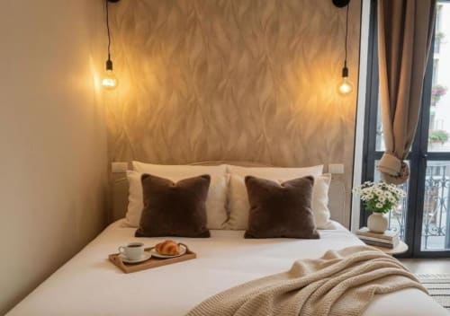 Camera da letto moderna a Milano con letto matrimoniale, cuscini in velluto marrone, luci a sospensione e vassoio colazione vicino alla finestra