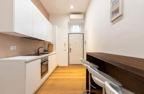 Cucina moderna nell'appartamento A Casa di Imma Milano con mobili bianchi, pavimento in legno e tavolo da pranzo vicino all'ingresso