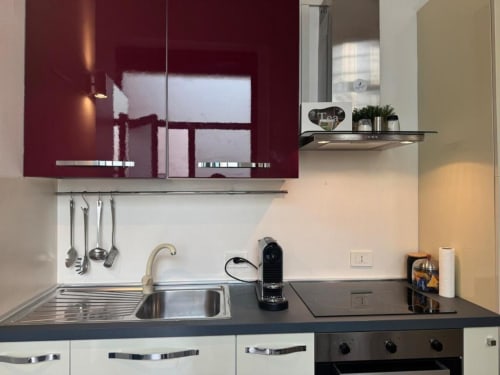 Cucina moderna in appartamento milanese con mobili bordeaux, lavello in acciaio inossidabile e piano cottura nero