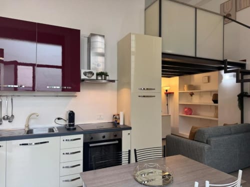 Moderno loft familiare a Milano con cucina open-plan, zona pranzo e soggiorno con divano grigio e scaffalature integrate.