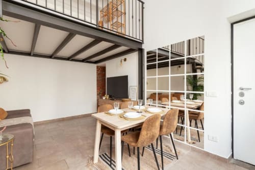 Zona pranzo del loft milanese moderno con travi a vista, scaffalature bianche e tavolo preparato presso Casa di Imma