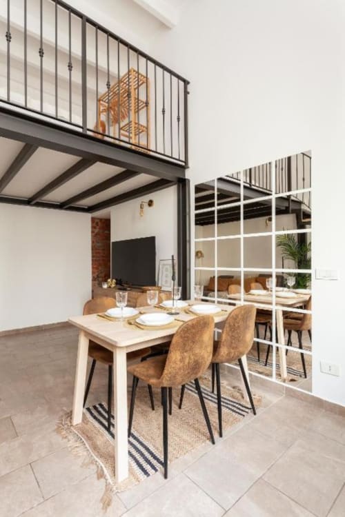 Zona pranzo loft contemporaneo presso A Casa di Imma Milano con tavolo bianco, sedie beige, soppalco e scaffalature a griglia