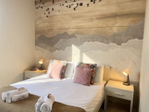Luminosa camera da letto in appartamento milanese con murale montano, cuscini rosa, biancheria bianca e illuminazione calda vicino a Bocconi