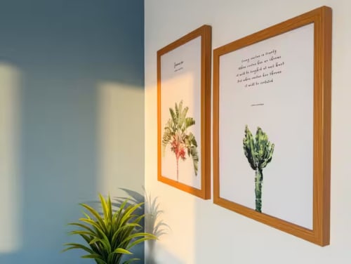 Due illustrazioni botaniche incorniciate con cornici in legno su parete bianca in appartamento milanese, pianta in vaso sottostante