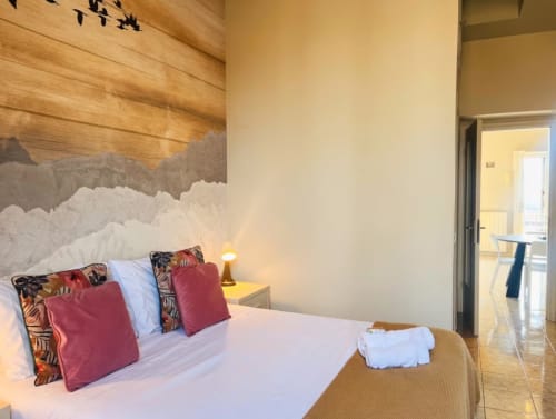 Camera da letto moderna dell'appartamento A Casa di Imma Milano con testiera paesaggio montano, cuscini bordeaux e porta in vetro verso