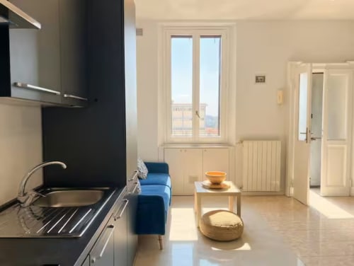 Moderno appartamento a Milano vicino a Bocconi con cucina a vista, sedia blu e luce naturale dalle porte-finestre del balcone
