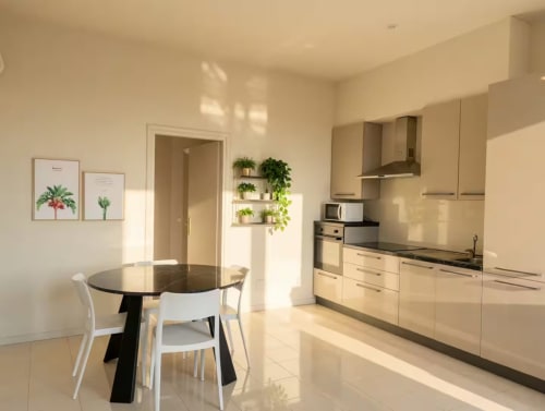 Moderna cucina e sala da pranzo in appartamento a Milano vicino a Bocconi con mobili color crema, tavolo tondo nero e scaffali con piante