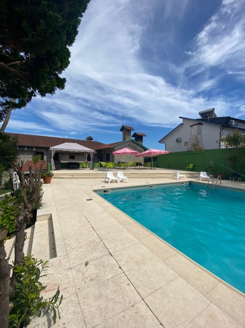 Área da piscina do hostel Casa Augusta em Braga, Portugal com água turquesa, espreguiçadeiras, guarda-sóis rosa e pátio de pedra