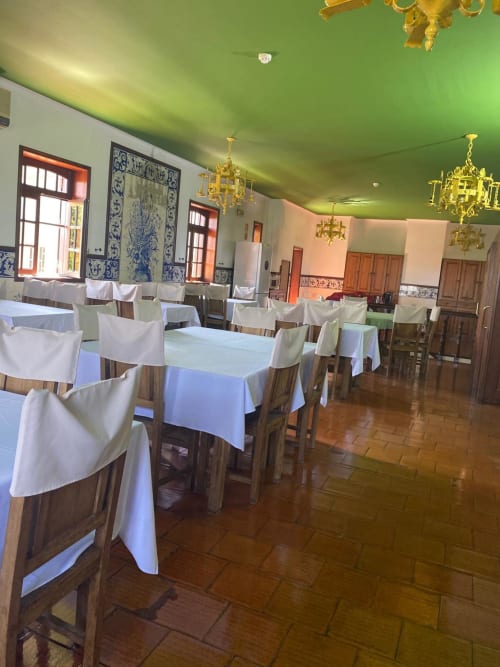 Sala de refeições do hostel Casa Augusta em Braga com mesas com cortinas azuis, cadeiras de madeira, teto verde e lustres dourados.