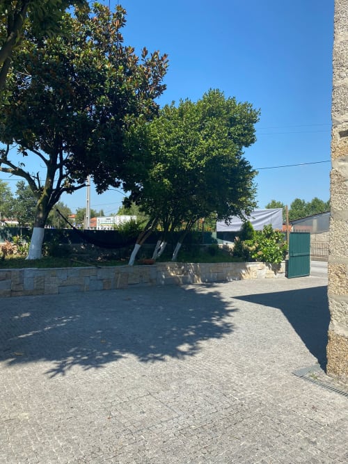 Pátio da pousada Casa Augusta em Braga, Portugal com muros de pedra, portão verde e árvores centenárias num dia ensolarado