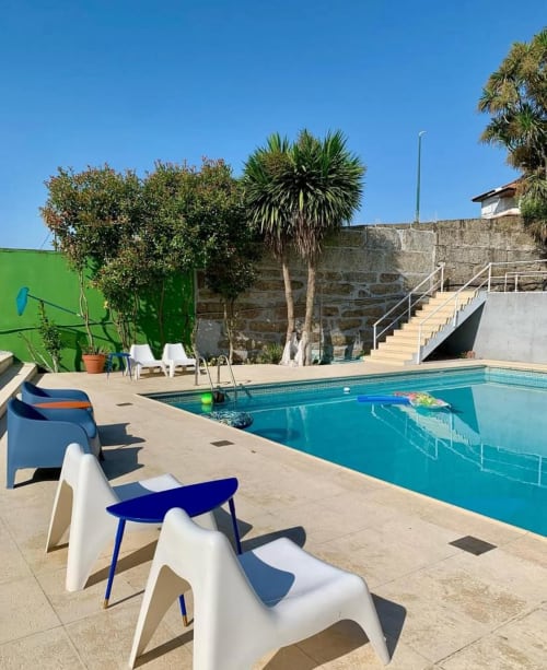 Área de piscina do hostel Casa Augusta em Braga com cadeiras brancas modernas, água turquesa, palmeiras e muros de fortaleza de pedra