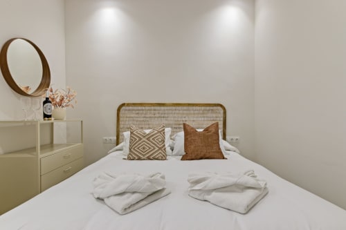 Ayma Suite bedroom with rattan headboard, white bedding, decorative pillows, and round mirror in Alhaurín de la Torre