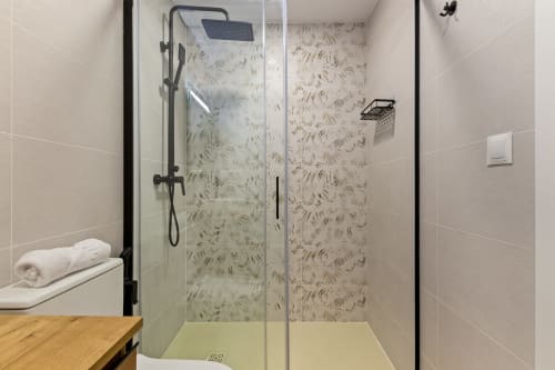 Modern shower with glass enclosure and leaf-patterned tile walls in Ayma Suite apartment, Alhaurín de la Torre