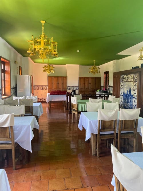 Sala de refeições do albergue Casa Augusta em Braga com teto verde, mesas de madeira e lustres elegantes