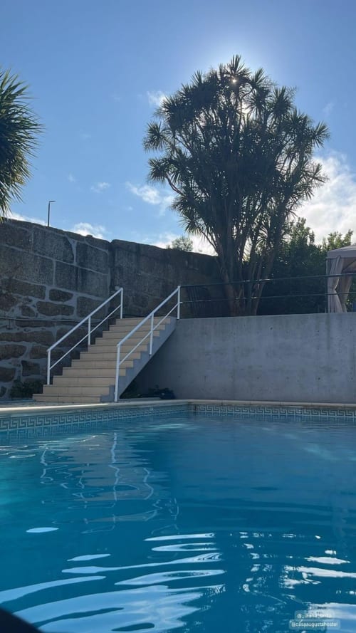 Piscina da pousada Casa Augusta em Braga, Portugal, com palmeira e escada de pedra sob céu azul