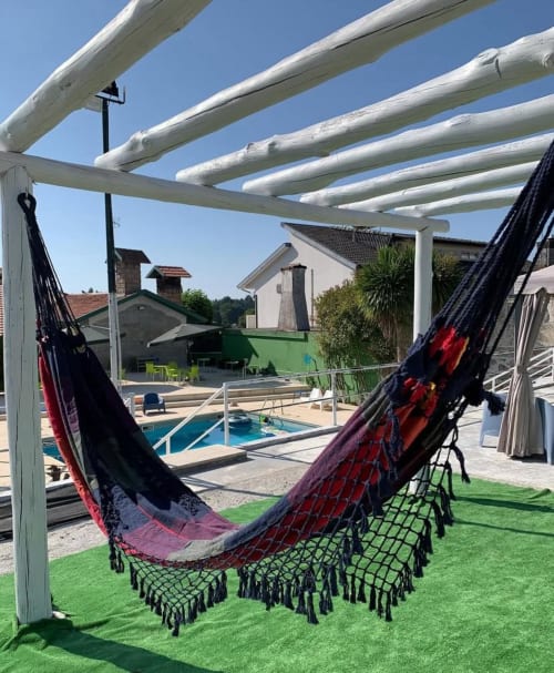 Redes coloridas com franjas sob pérgola branca com vista para a piscina na Casa Augusta, Braga, Portugal