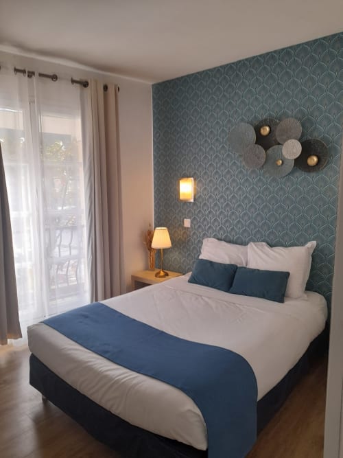 Lits jumeaux aux draps blanc et bleu à l'Hôtel le Vauban de Carentan, tête de lit à motifs bleu canard, lampe de chevet et porte vitrée