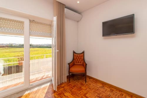 Quarto moderno de albergue em Esposende com piso de madeira, poltrona laranja, TV na parede e vista para a zona rural