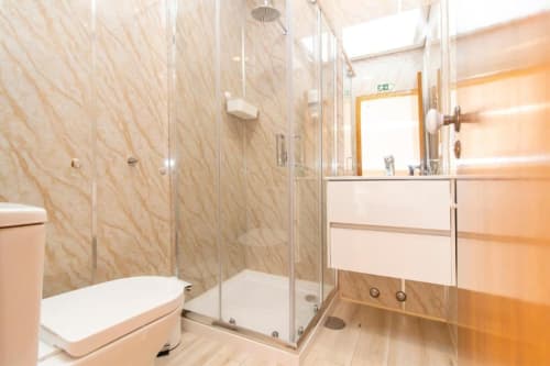 Banheiro moderno no hostel Sleep & Go em Esposende com box de vidro, pia branca e azulejos bege